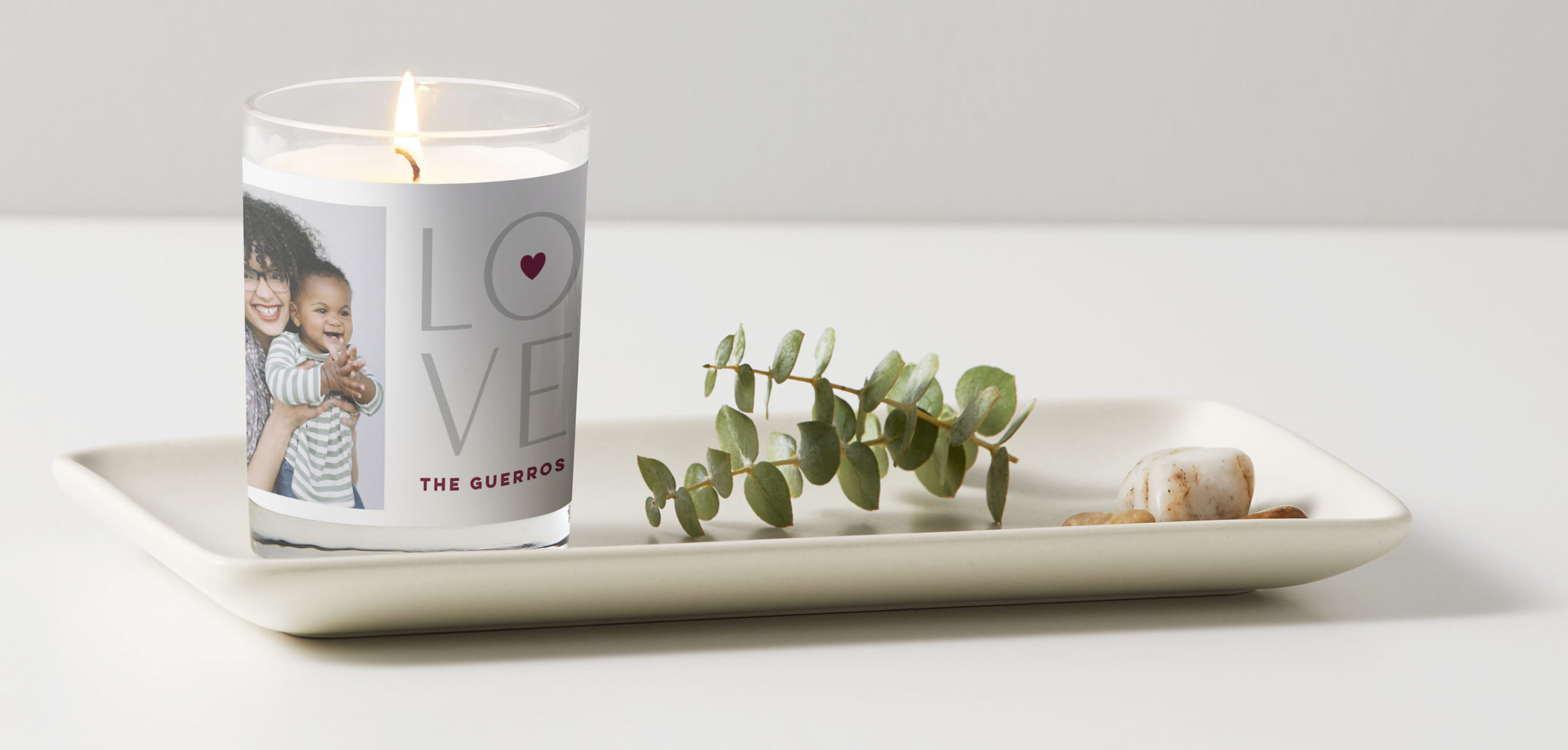Custom candle with the word love written on it placed on a cream tray featuring a mother and her child